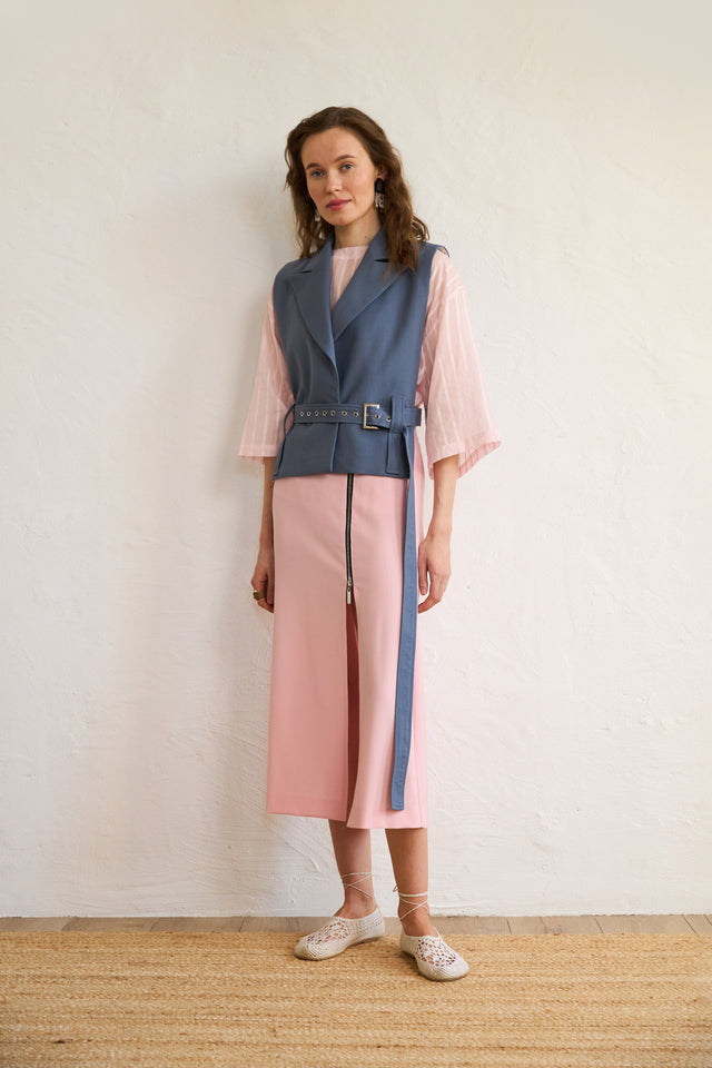Woman wearing a two-tone dress with a blue vest and pink skirt against a plain background.