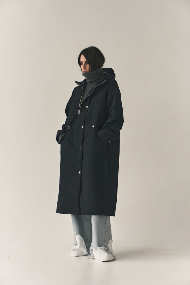 Person wearing a black coat on a plain background