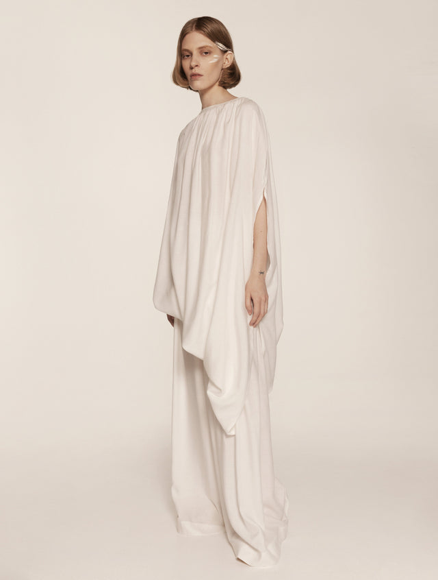 Woman wearing a flowing white dress on a plain background