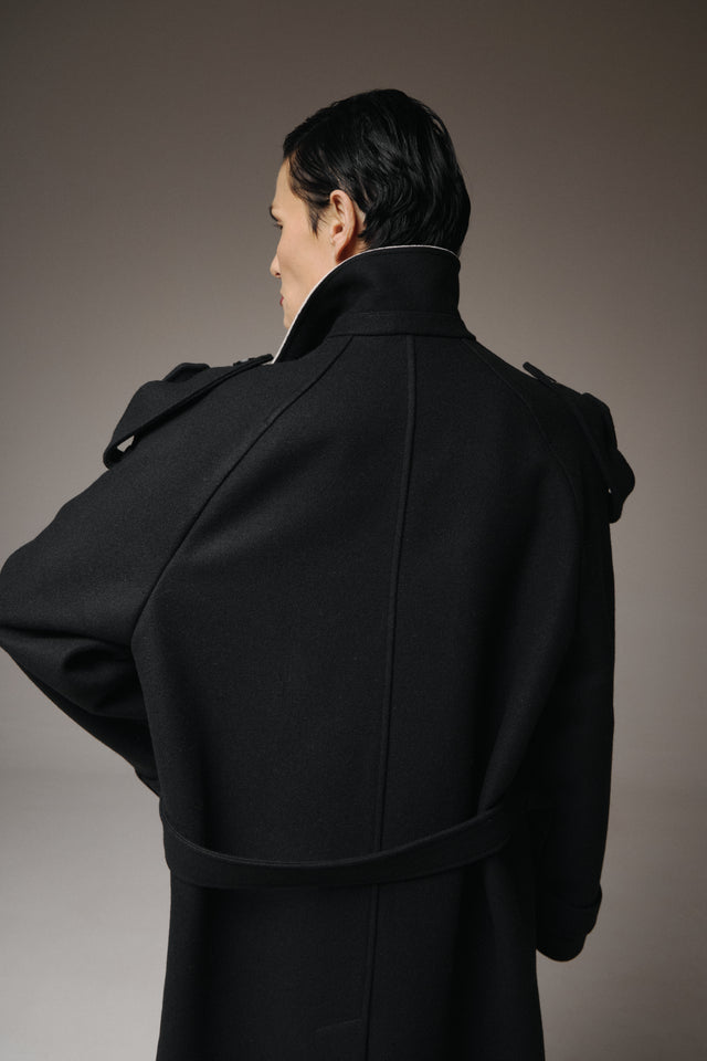 Person wearing a black coat against a gray background