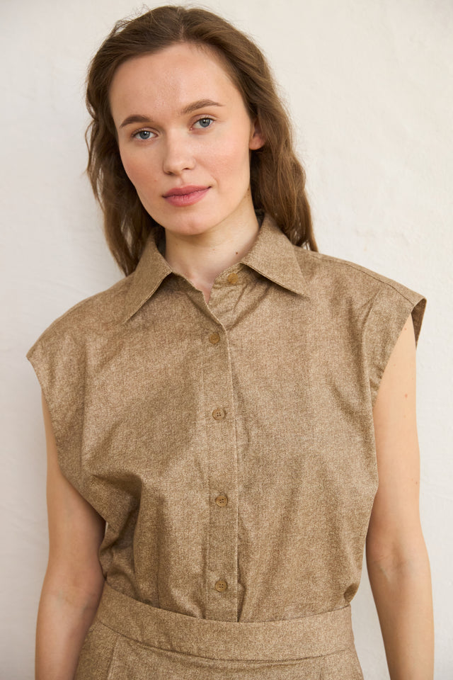 Woman wearing a brown sleeveless blouse against a plain background