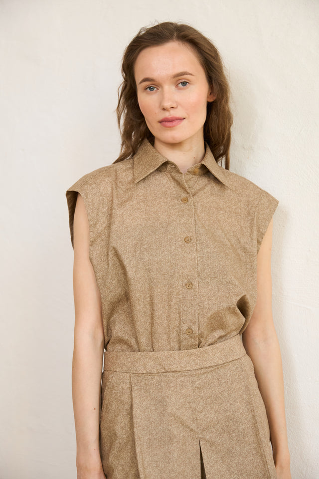 Woman wearing a brown sleeveless shirt and skirt set against a plain background