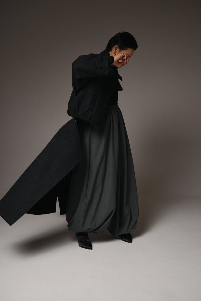 Person wearing a long black coat and skirt against a plain background