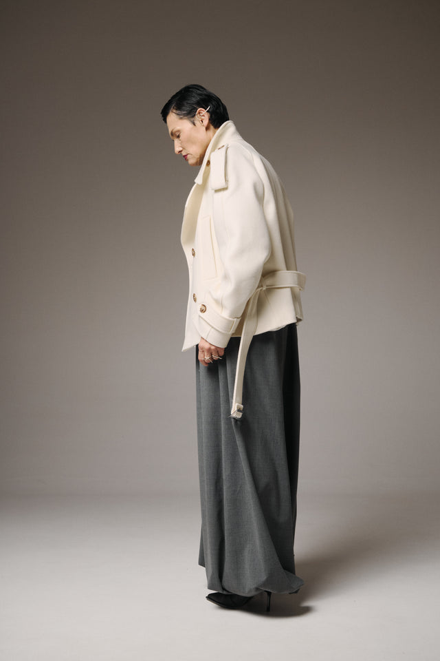 Person wearing a beige coat and gray pants against a plain background