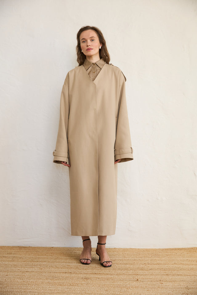 Woman wearing a beige long coat against a plain background